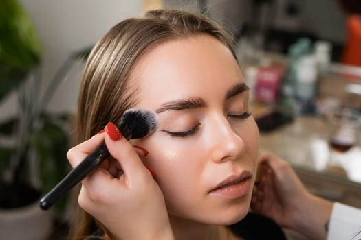 Woman makeup artist strategically layers facial powder on cheek. Professional provides young client durable base withstanding rigors of day