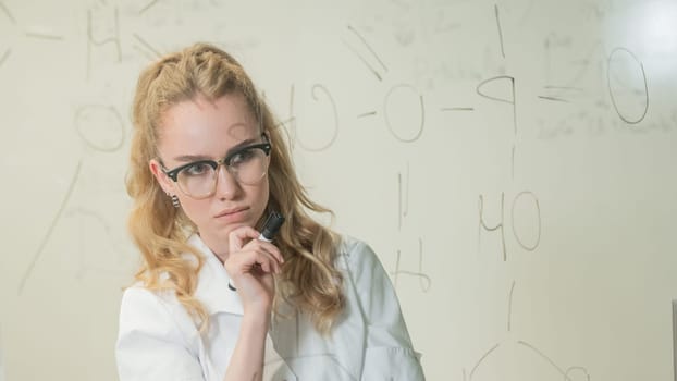 A Caucasian woman in a medical gown thinks and finalizes formulas on a transparent wall