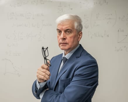 Mature man stands at a white board with written formulas