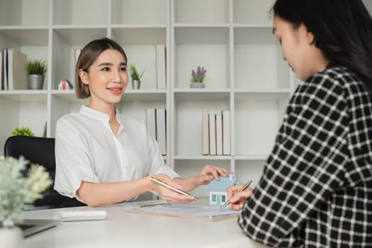 Two Asian businesswomen signing real estate documents at office desk. Concept of real estate agreement and professional consultation.