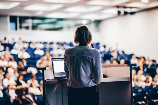 Female speaker giving a talk on corporate business conference. Unrecognizable people in audience at conference hall. Business and Entrepreneurship event