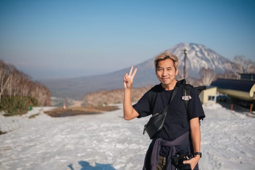 Smiling man with camera posing on snowy mountain. Concept of travel and photography.