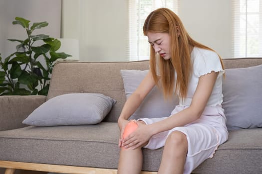 Asian woman experiencing knee pain at home. Concept of joint discomfort, pain relief, and health issues.