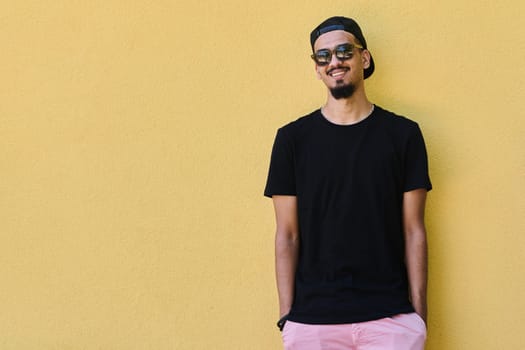 A depiction of urban coolness: a Middle Eastern teenager leaning against a yellow wall, exuding confidence in casual attire.