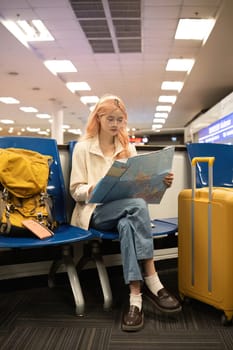 Asian woman reading map and using smartphone in airport. Concept of travel, navigation, and preparation..