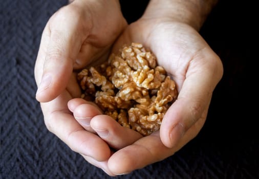 Above photo of group of nuts in the hands of a young man. Dark background. Fruits and nuts. Omega 3 source