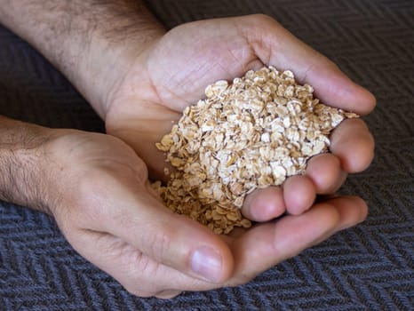 Close up picture of hands of a young man rolled oats falling from one hand into another. Grey background. Healthy food. Vegan
