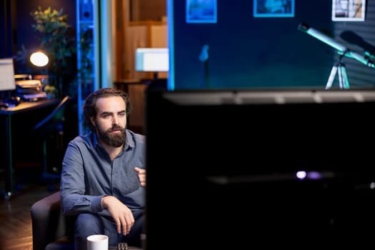 Cord cutter sitting on couch in front of TV displaying streamed news program. Person at home watching television screen showing video on demand channel with newscast coverage