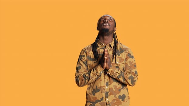 African american person praying to Jesus in studio, being spiritual and showing belief in God over orange background. Young adult saying prayer and feeling hopeful, religious man smiling.