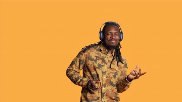 Playful adult playing air guitar on camera and singing, having fun with music on headphones. African american guy pretending to play imaginary musical instrument, listening to songs.