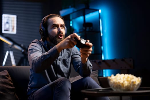 Man showing surprise facial expression while playing videogames on gaming console with teammates. Player acting shocked after being defeated by foes in game, discussing with friends through headset