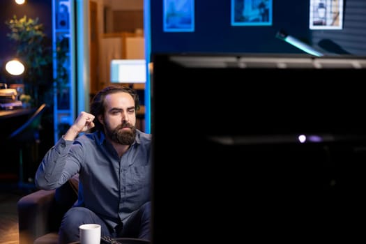 Fan satisfied by seeing favorite team win while watching live sports event broadcasted on TV, clutching hands. Supporter pleased with own club achievement after getting victory in football competition