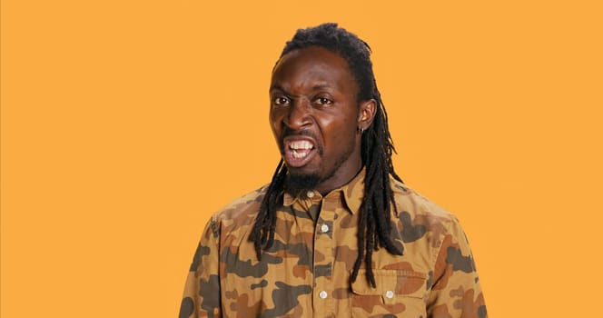 Confident adult screaming in front of camera in studio, feeling furious and angry. African american person showing rage and yelling, aggressive mad guy with dreads. Handheld shot.