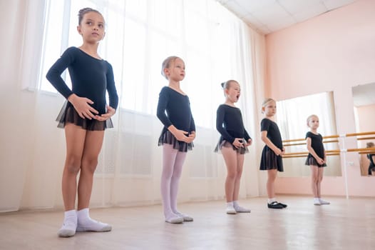 Cute little girls in black swimsuits and tutu practice ballet in class