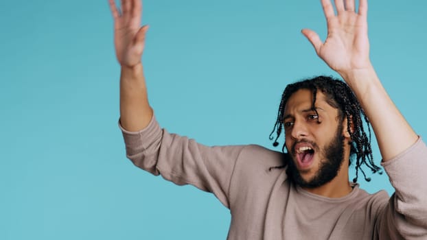 Ecstatic Middle Eastern person having fun, throwing hands in air, celebrating, enjoying leisure time. Joyful BIPOC man entertaining himself doing upbeat gesturing, studio background, camera B