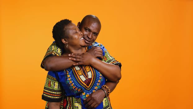 Cute african american people embracing on camera, holding each other and expressing their true love. Ethnic romantic husband hugging his wife in studio over orange background.