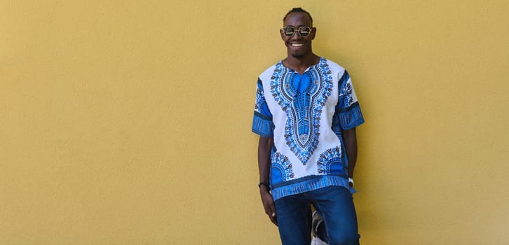 A vibrant portrait of an African American teenager proudly wearing traditional Sudanese clothing against a striking yellow background.