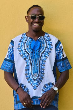 A vibrant portrait of an African American teenager proudly wearing traditional Sudanese clothing against a striking yellow background.