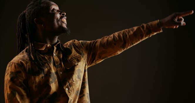 African american guy cheers for someone in studio, supporting and encouraging person over black background. Adult feeling confident and optimistic, celebrating victory and triumph. Handheld shot.