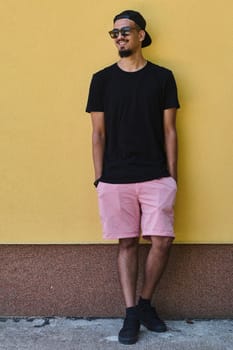 A depiction of urban coolness: a Middle Eastern teenager leaning against a yellow wall, exuding confidence in casual attire.