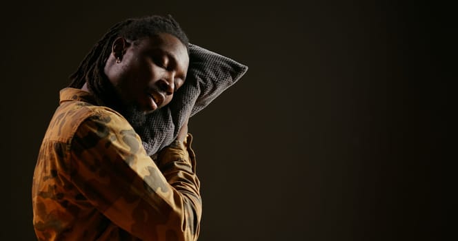 Sleepy person napping with his pillow while he is standing, falling asleep on camera because of burnout and fatigue. Tired african american guy feeling exhausted and overworked, insomnia concept.