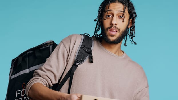 Portrait of BIPOC courier delivering pizza order to client. Delivery part time worker using thermal backpack to store food and bring it to customer, isolated over studio background, camera B