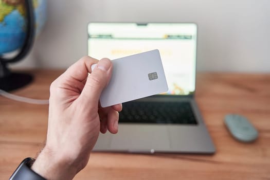 A person is holding a credit card in front of a personal computer with a laptop screen. They are using the touchpad to make a gesture