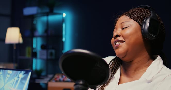 Zoom in on african american woman streaming podcast using vlogging camera during live political debate on vlog channel. Internet show presenter in dimly lit studio, close up