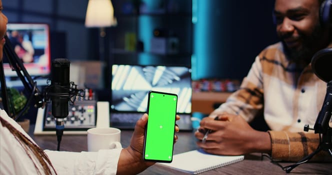 Isolated screen cellphone in front of show presenter recording podcast, enjoying cup of coffee and nice conversation with guest. Chroma key phone in studio used for live broadcast with woman