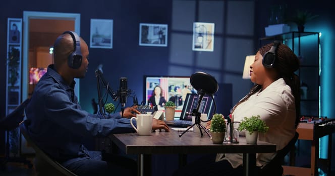 Show host recording podcast with guest, using analog mixer and professional mic in studio. Zoom out shot of man setting up audio device for live broadcast with woman, ensuring flawless sound quality