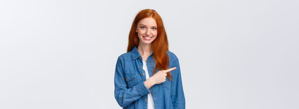 Here what need. Cheerful redhead woman in denim shirt, pointing finger left copy space, smiling recommend good product, review service, indicating website, standing white background.