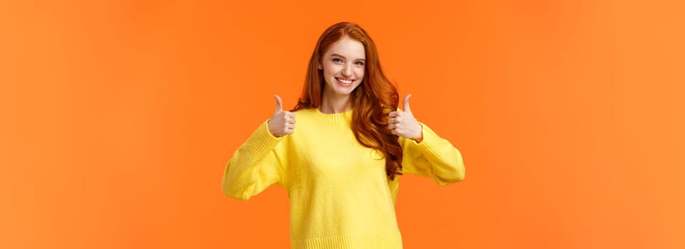 Confident and caring good-looking redhead sister rooting for sibling, saying yes, approving choice, recommend product, show thumbs-up and nod acceptance, smiling positive reply, orange wall.