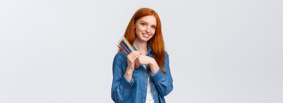 Good-looking charismatic dreamy redhead female in denim shirt, looking camera thoughtful and imaging, want draw something, have design project in mind, holding colored pencils, white background.
