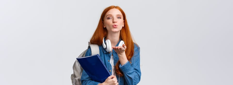 Lovely and tender, sensual redhead college girl, sassy student with red hairstyle, send air kiss, blowing mwah at camera passionately, holding backpack and folder with documents.