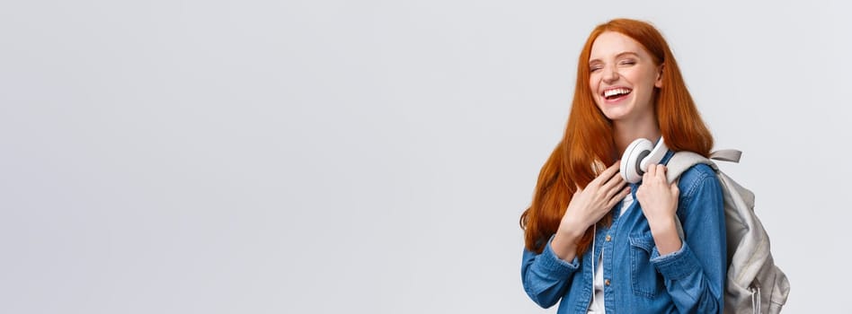 Charismatic and cheerful, lovely friendly redhead girl laughing over girlfriend joke as heading back campus from university classes, having fun chuckle with closed eyes, smiling, holding backpack.