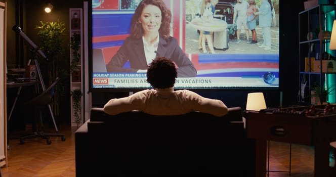 Man in home theatre watching huge TV screen showing news broadcast reportages on family trips. Zoom in shot on cord cutter looking at streaming service travelling channel on widescreen television set