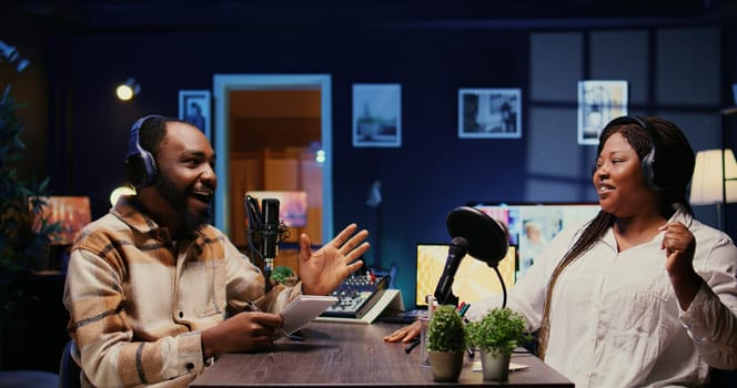 Vlogger show host interviewing guest in neon lights ornate studio, following questions written on paper. Man filming online podcast episode with woman, discussing about personal life