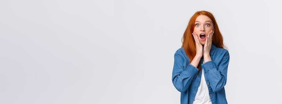 Oh my gosh, amazing. Surprised speechless redhead woman standing starled and shocked, touch face, drop jaw and stare camera fascinated, got job, won prize, standing white background.