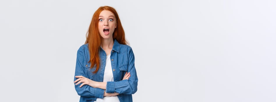 Omg, no way, unbelievable. Impressed and surprised, curious redhead girl dropping jaw from amazement, lose speech, staring astonished, standing astounded, found out awesome news, white background.