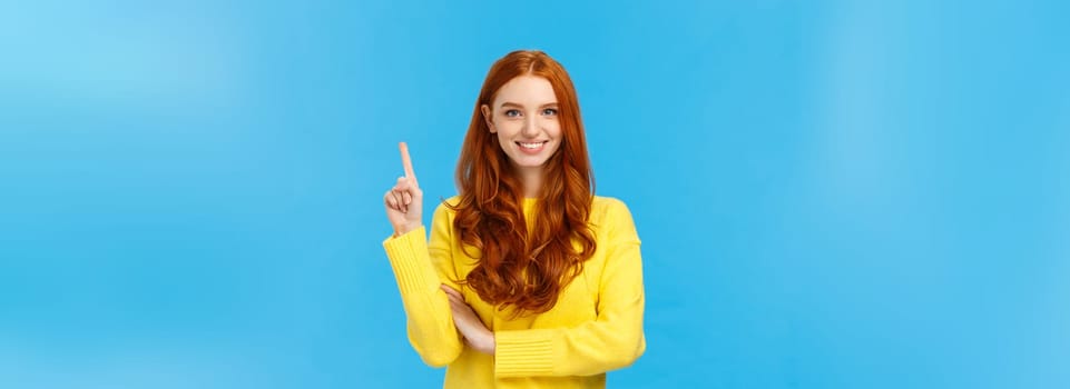 Attractive confident and charismatic caucasian redhead female in yellow sweater, showing number one, order product, being first, smiling satisfied and assertive, standing blue background.