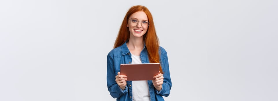 Education, people and teamwork concept. Cheerful pretty redhead millennial female coworker introducing project to team, holding digital tablet, wearing glasses, smiling at camera.