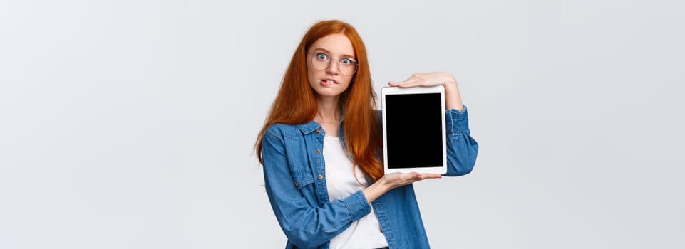 Cant resist temptation, add to cart now. Tempting and curious good-looking excited redhead woman in glasses, biting lip desire buy something online, showing digital tablet screen, white background.