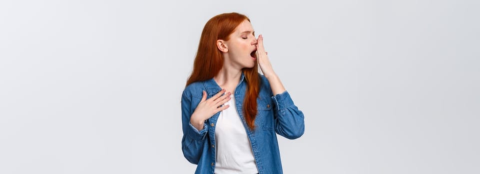 Waist-up portrait lovely redhead girl want sleep, feeling tired or bored, turn head away and yawn, cover opened mouth with palm, yawning over white background after boring class, white background.