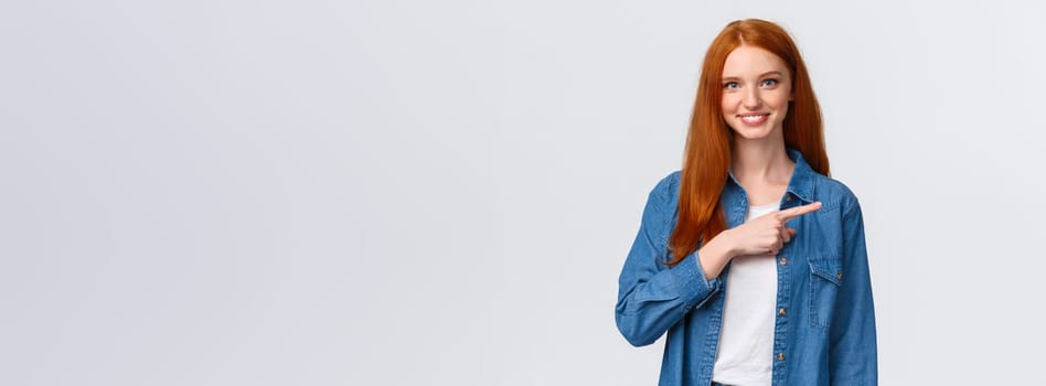 Waist-up portrait friendly smiling, happy redhead confident female student in denim shirt, showing where good courses online, pointing finger right and grinning, invite join, white background.