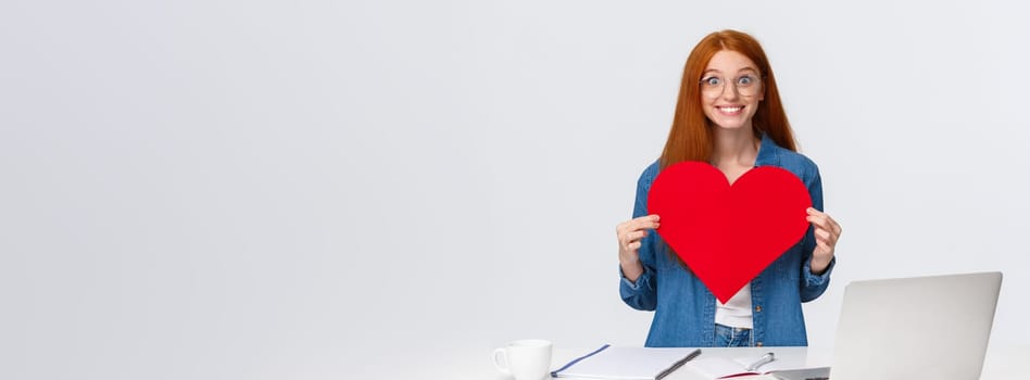 Cheerful and excited cute girlfriend with red hair, cant wait give big red valentines heart to boyfriend, showing sympathy, confess in love, celebrating lovers day, standing white background.