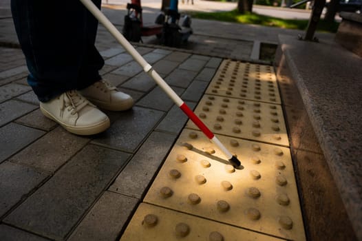 Close-up of female foot, walking stick and tactile tiles. Blind woman climbing stairs using a cane