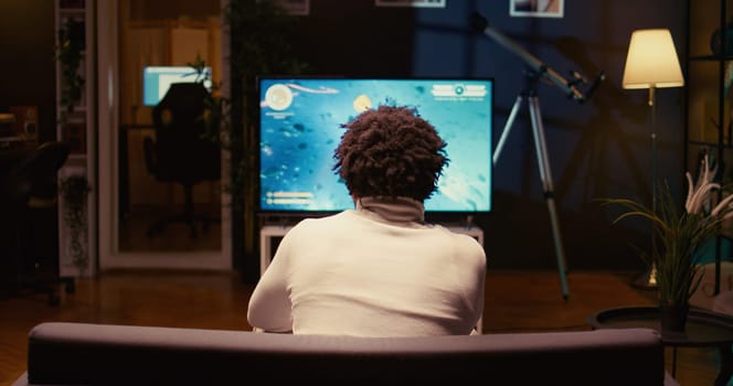 BIPOC gamer playing classic arcade space shooter videogame on modern smart TV, shooting asteroids. Jib down shot of man using gaming console to solve missions in singleplayer game