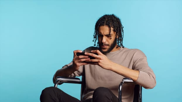 Gamer with disability upset after receiving game over screen on smartphone display. BIPOC man in wheelchair feeling sad after losing videogame, playing on mobile phone, camera A