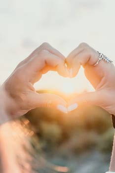 A woman's hand is holding a heart shape, with the sun shining on it. Concept of love and warmth, as the sun symbolizes happiness and positivity. The heart shape represents the bond between two people