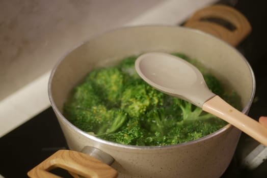 Fresh broccoli boiling in a pot on a stove with a wooden spoon, showcasing healthy cooking preparation.